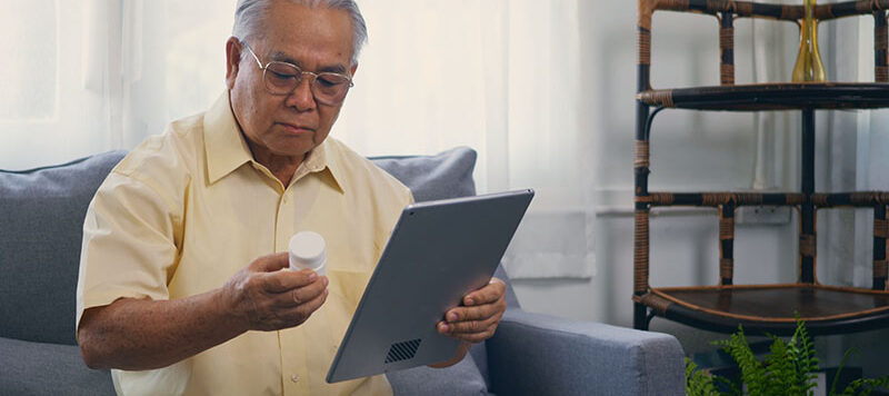 An elderly man holding a medication bottle and a digital tablet